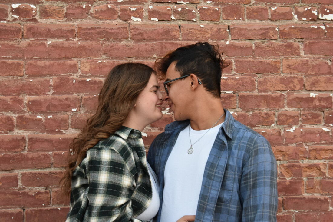 Photo of a man and a woman almost kissing in front of a brick wall
