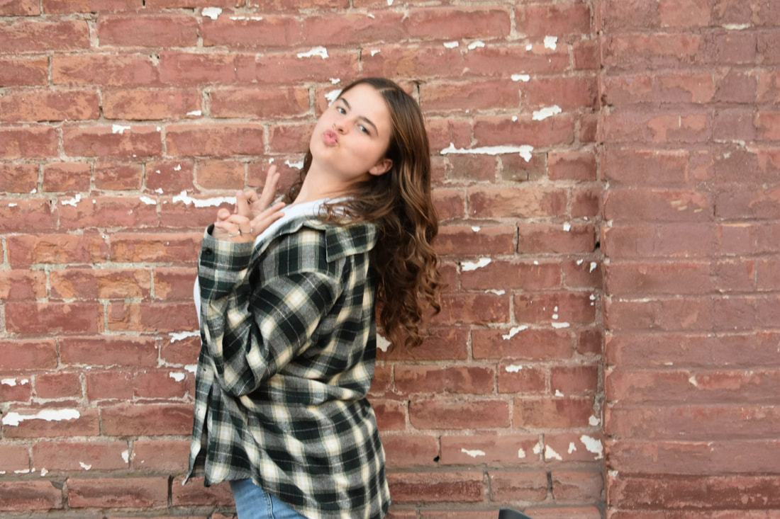 Photo of woman making a duck face and a peace sign in front of a brick wall